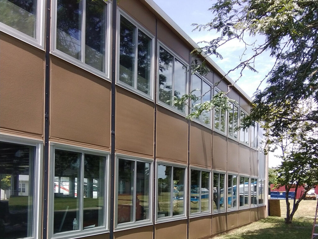 Side view of a modern brown building with large windows and greenery.