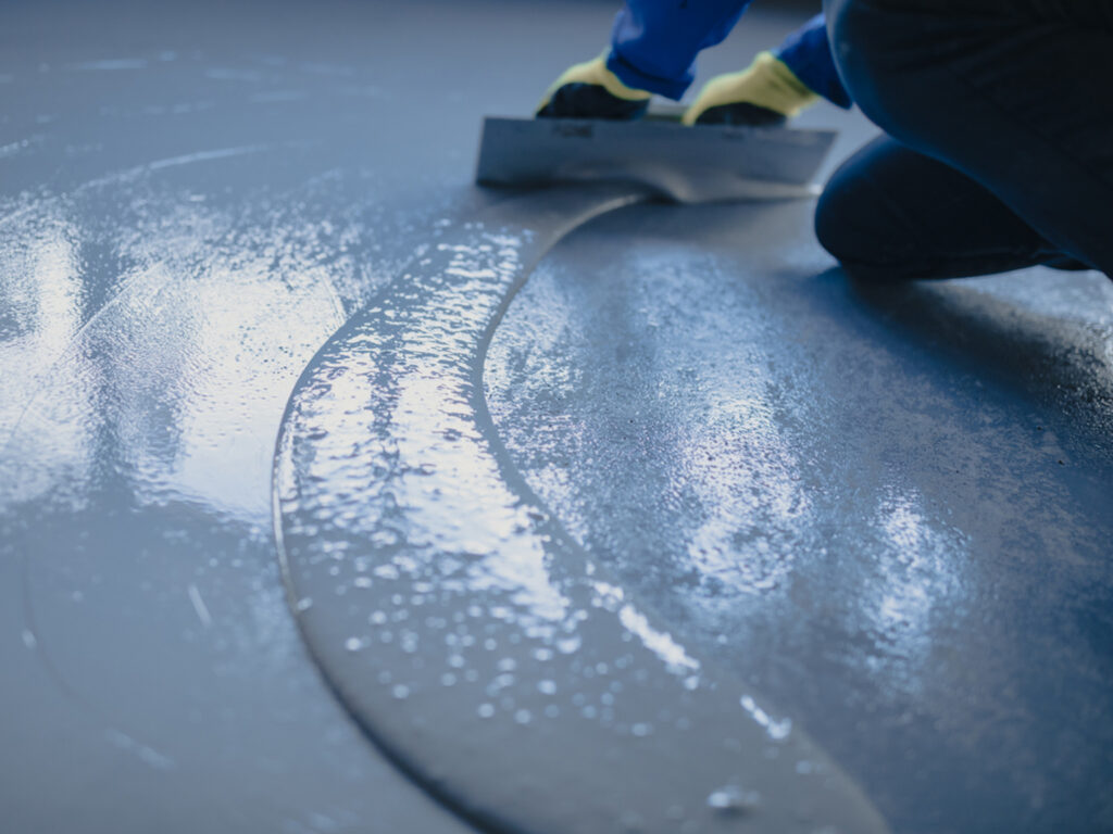 Worker using a trowel to evenly spread a layer of wet concrete.