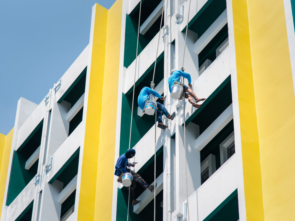 Workers painting a tall building facade in vibrant yellow and blue colors.