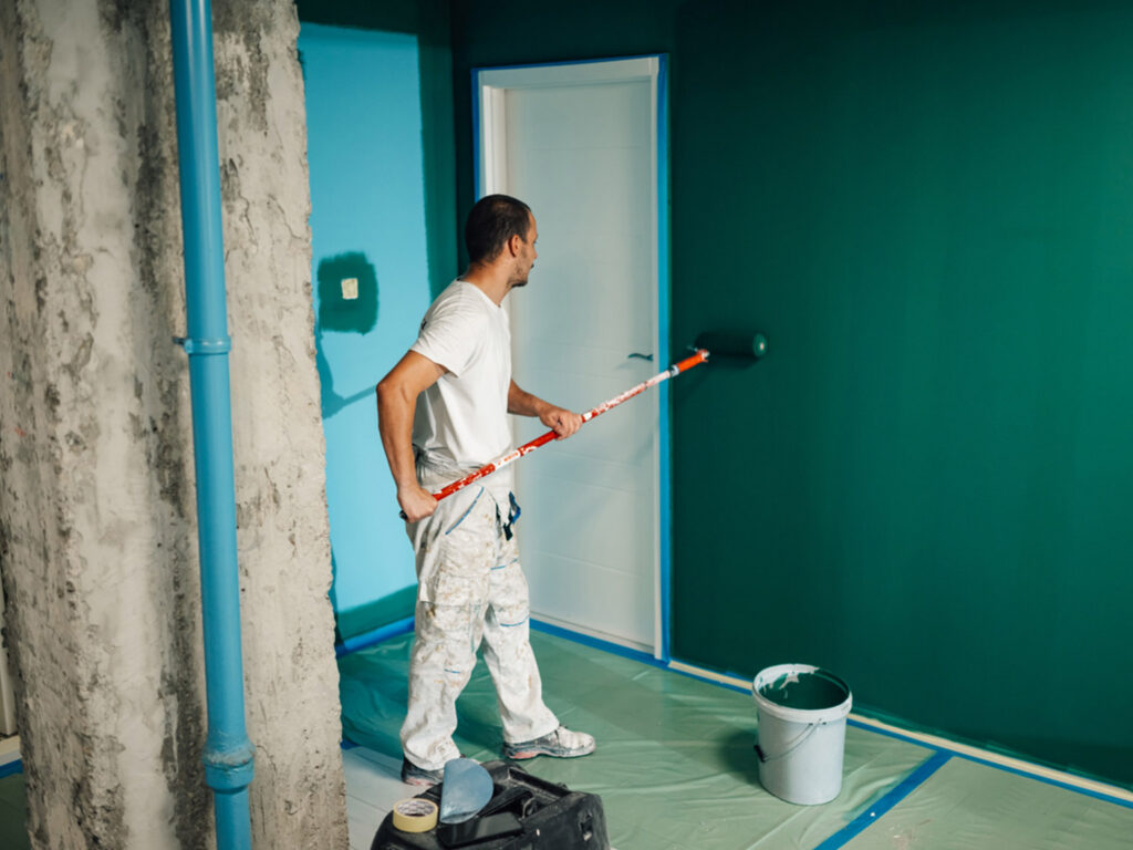 Man painting room wall with roller, vibrant green color application