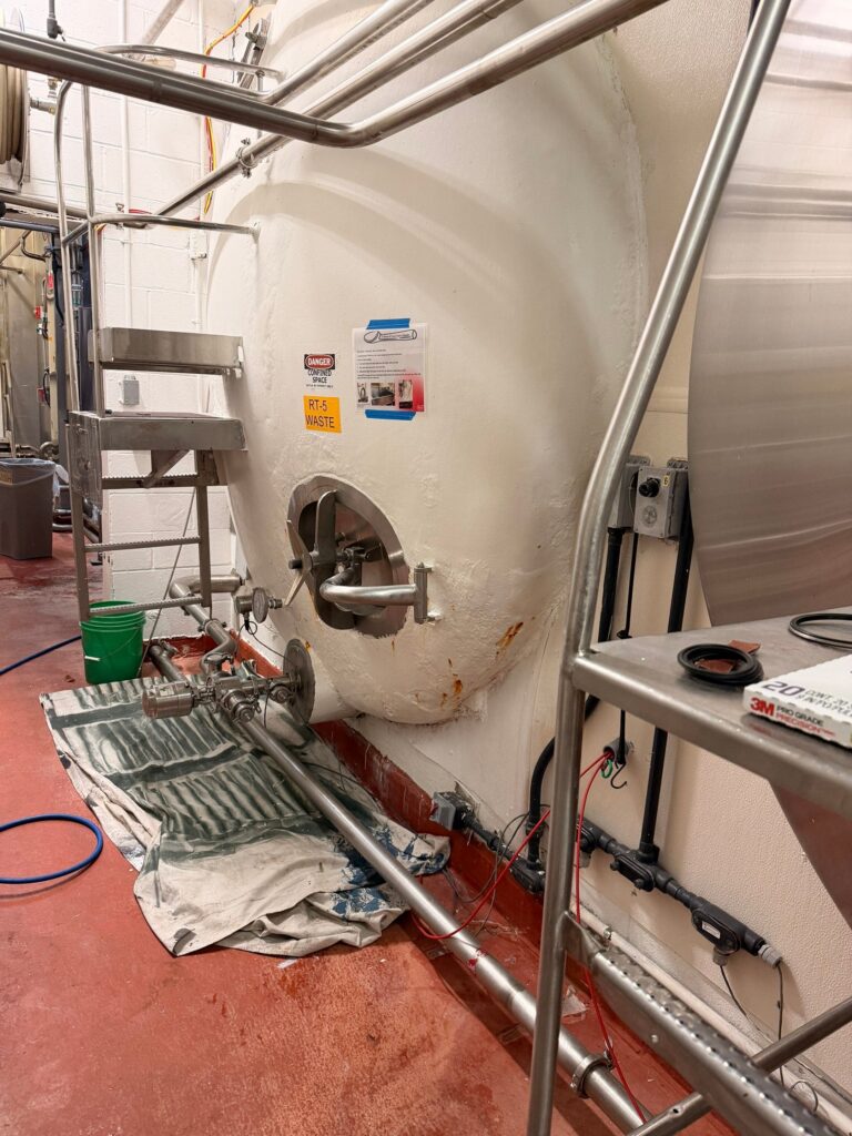 Industrial tank setup in a brewery with pipes and maintenance tools.