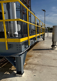 Industrial walkway with yellow railing under a clear blue sky.