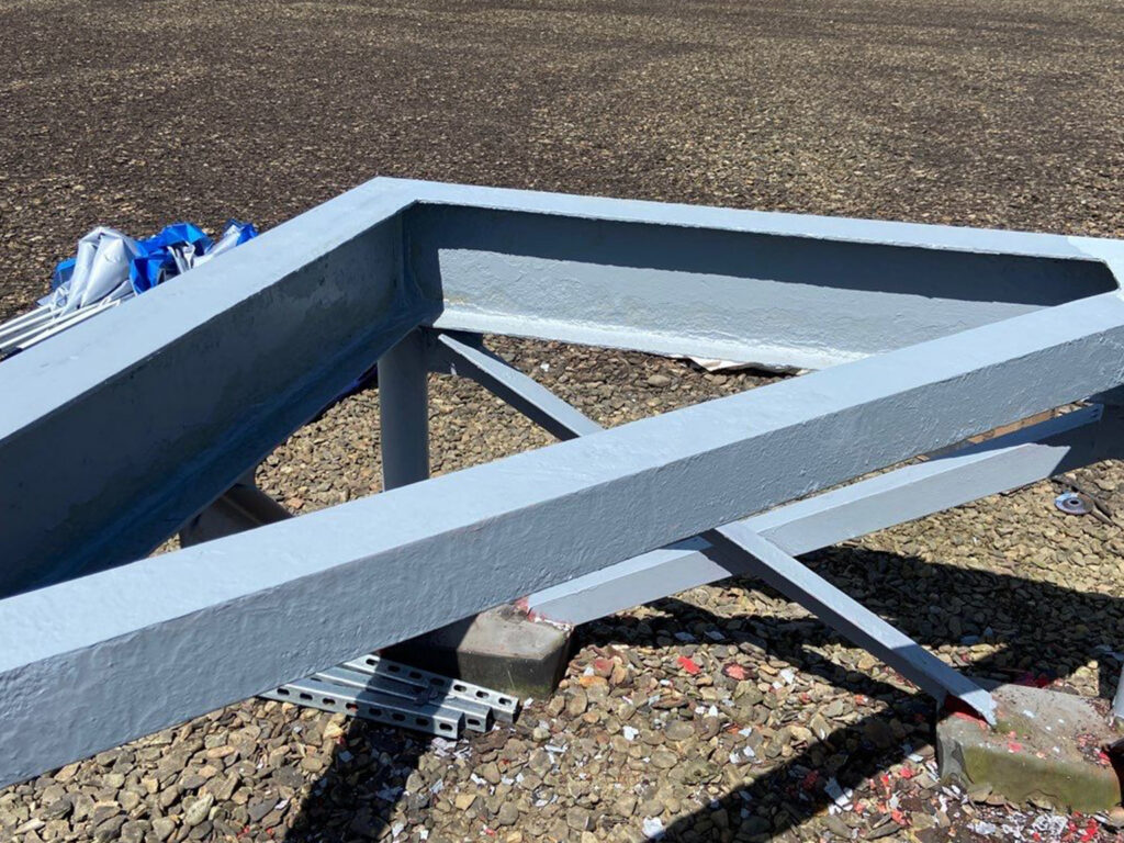 Gray metal framework resting on a rocky ground surface outdoors.
