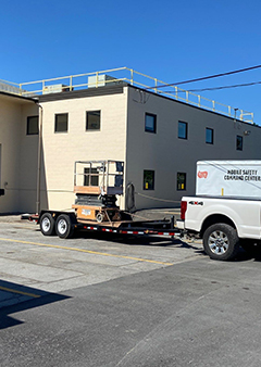 Truck towing a lift trailer parked near a beige industrial building.