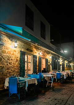 Outdoor night view of a charming restaurant with stone walls and blue chairs.