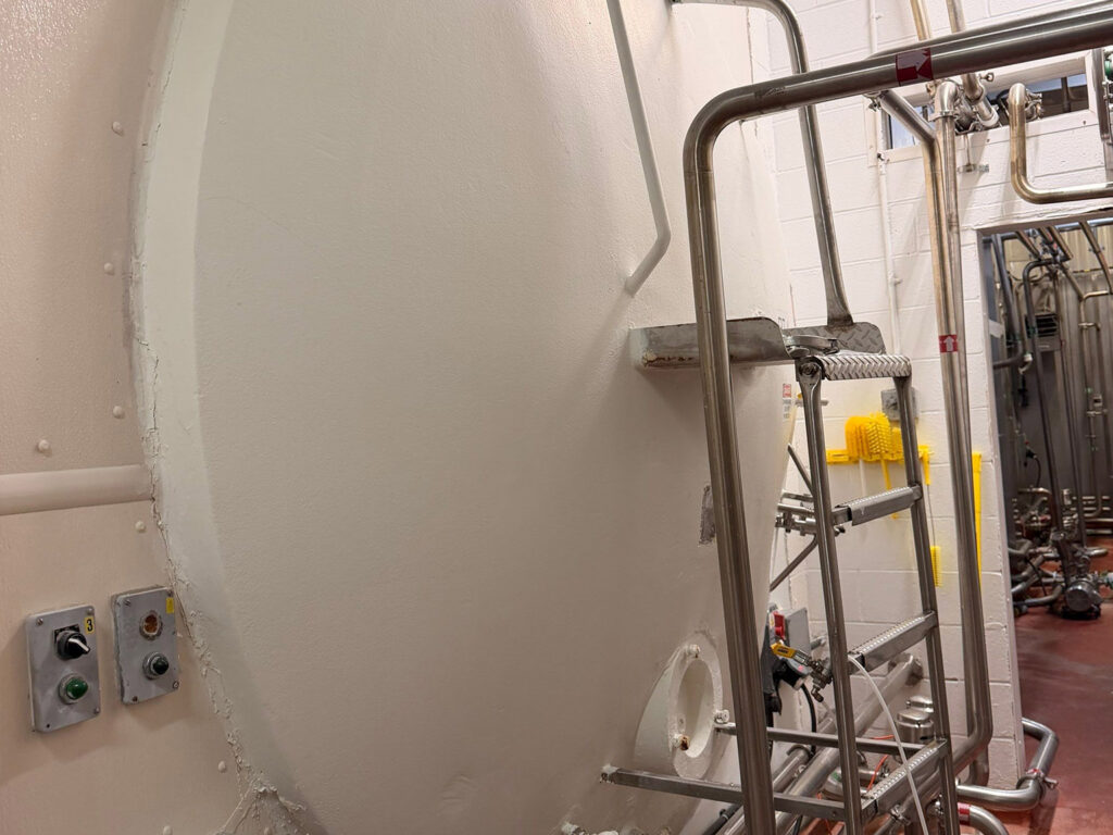 Industrial storage tank with ladder and control panel in factory setting.