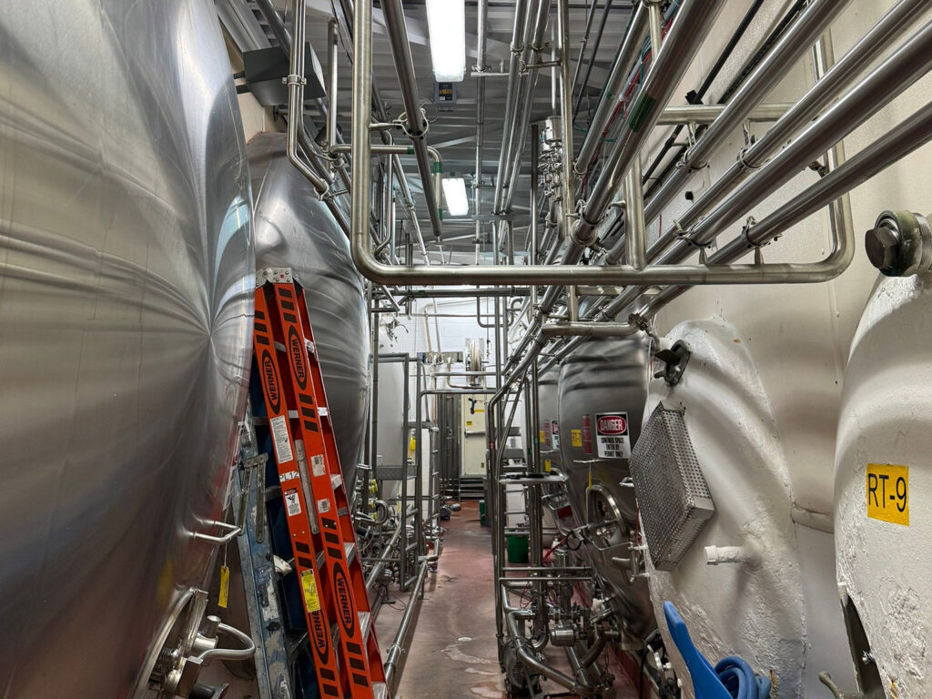 Industrial fermentation tanks with metal piping in a brewery facility.