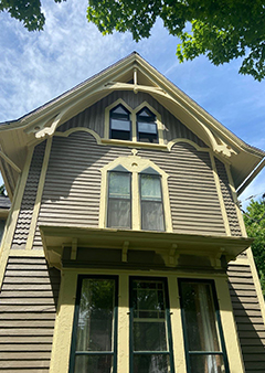 Historic two-story house with ornate gables under a blue sky.