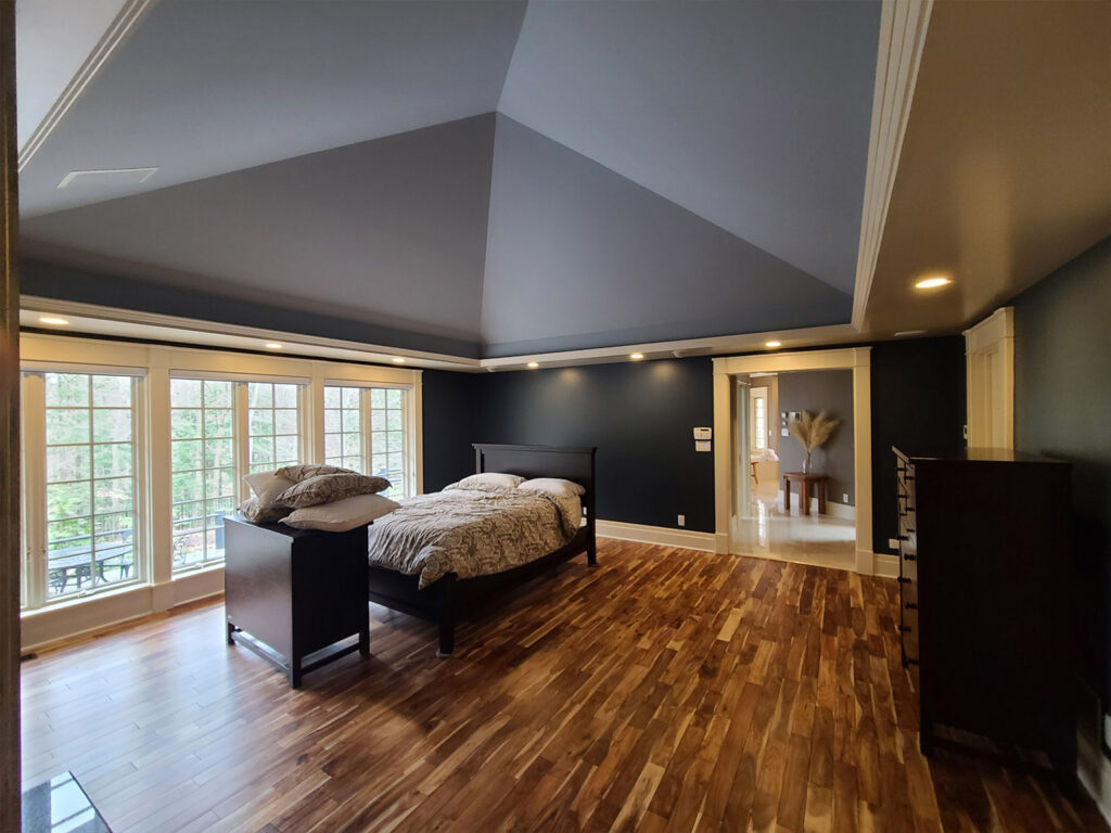 Spacious bedroom with dark walls and large windows overlooking greenery.