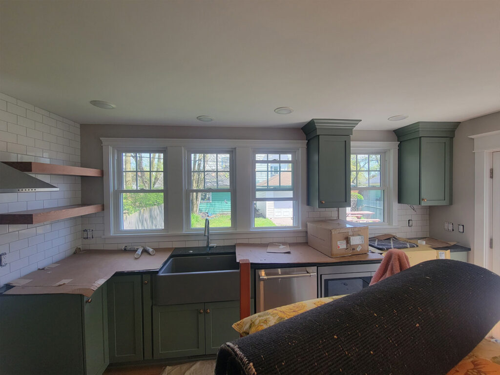 Modern kitchen under renovation with green cabinets and farmhouse sink.