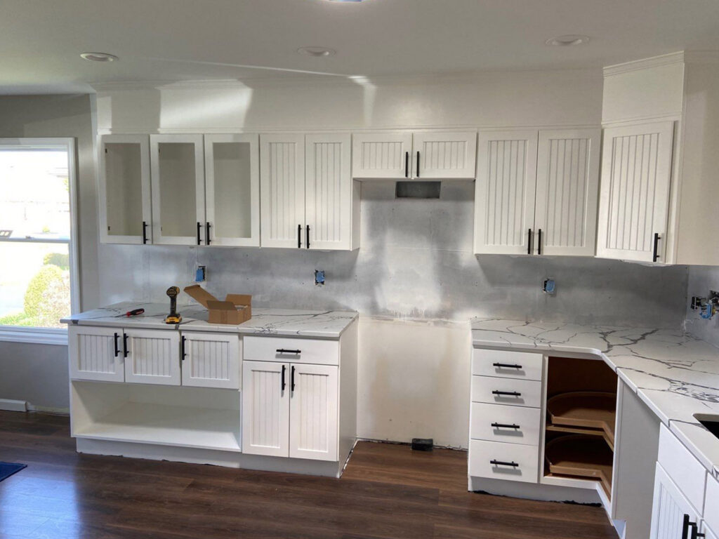 Modern kitchen under renovation with white cabinets and marble countertops.